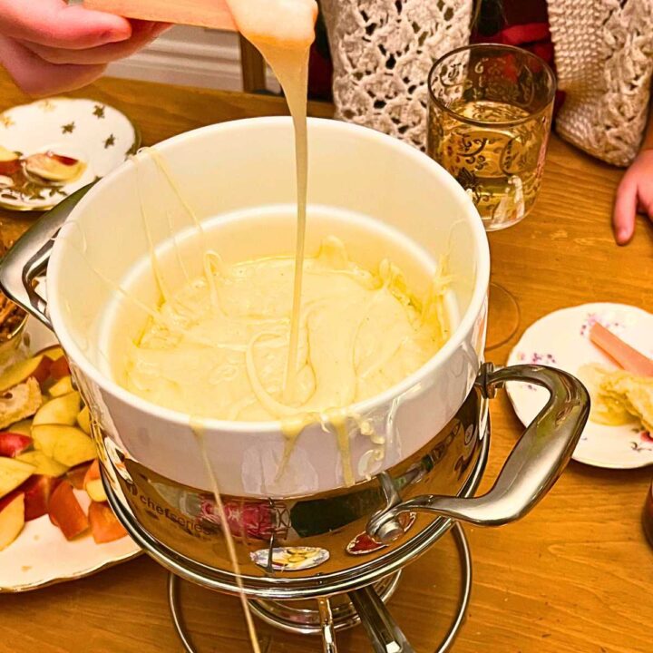 A child dipping a carrot stick into a cheese fondue.