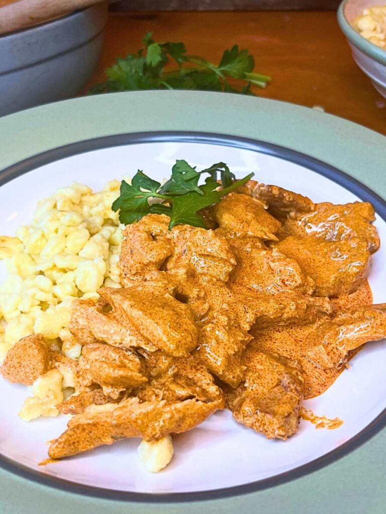 A green and white bowl with a serving of noodles and paprika chicken.