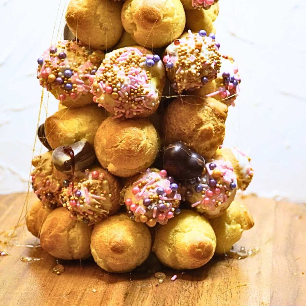 The bottom of a croquembouche decorated with pink sprinkles and chocolate hearts.