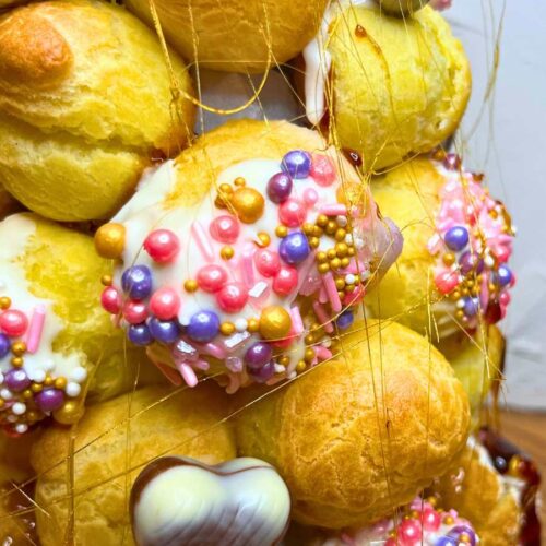 A close up look at a some profiteroles decorated with pink sprinkles. They are made into a croquembouche.