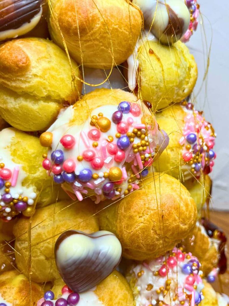 A close up look at a some profiteroles decorated with pink sprinkles. They are made into a croquembouche.