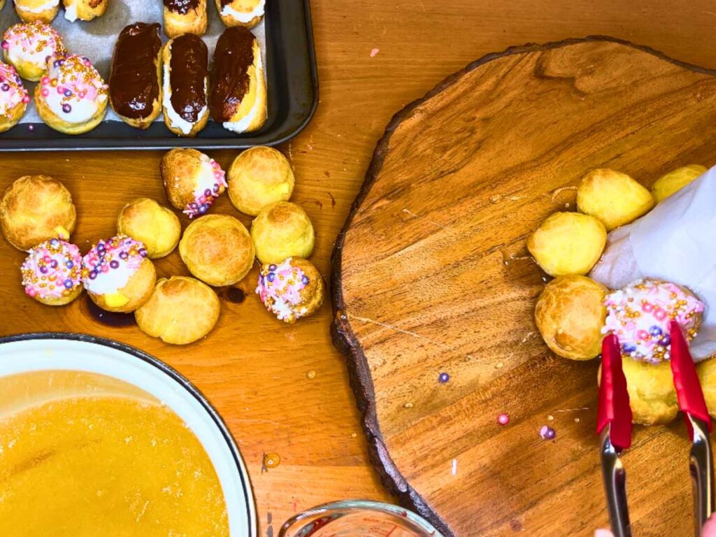 A woman is using caramel to glue profiteroles to a cone form.