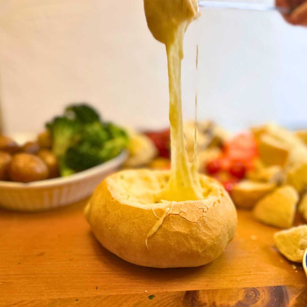 A piece of bread is being dipped into a bread bowl cheese fondue.