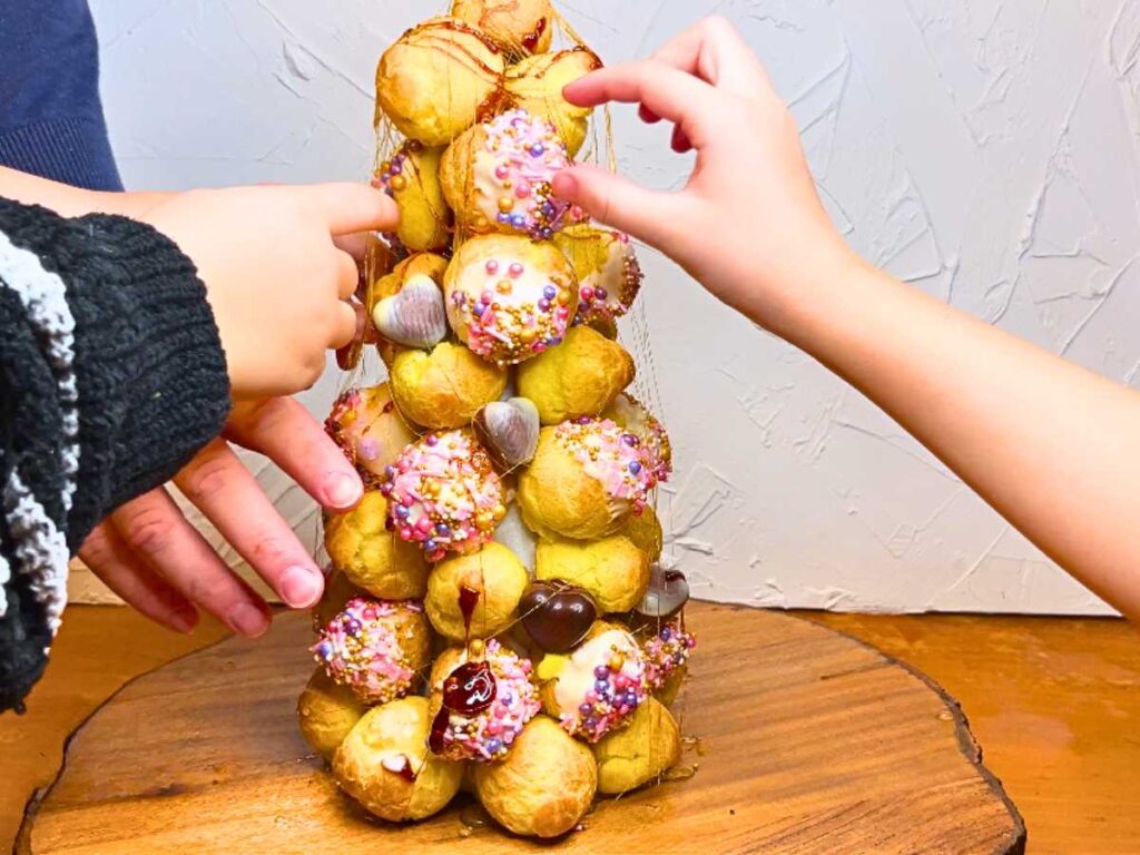 A group of people are grabbing profiteroles off of a croquembouche.