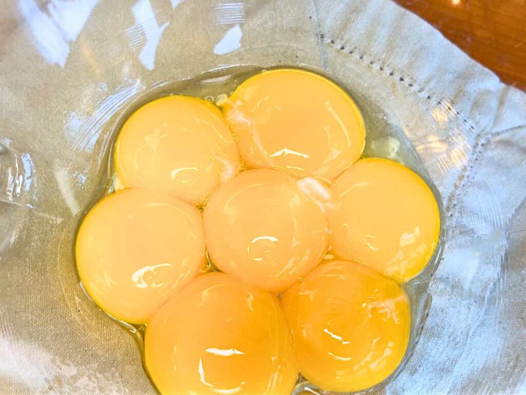 A glass bowl with 7 egg yolks inside.