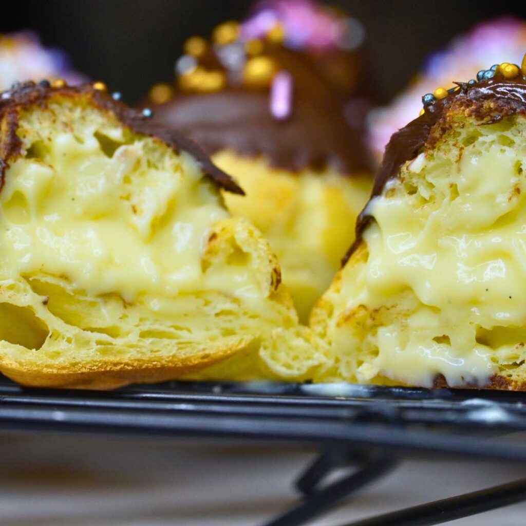 A close up look at a profiterole covered in chocolate. There is pastry cream inside.