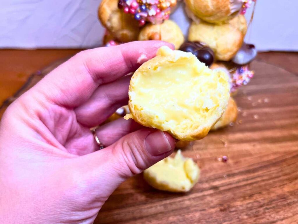 A woman is holding a profiterole, showing the inside pastry cream.