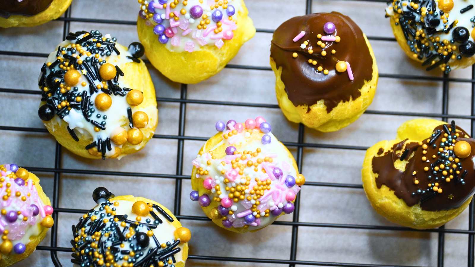 A group of decorated profiteroles on a wire rack. Some have white chocolate and some have semi-sweet chocolate coating.