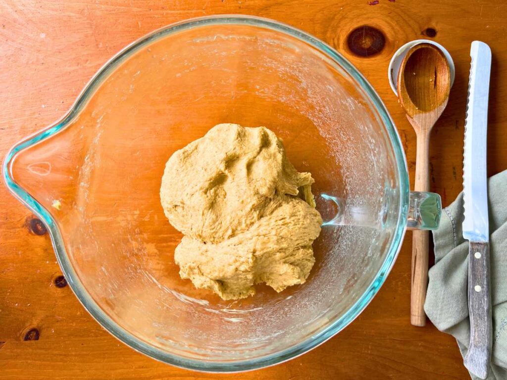 A glass bowl with a molasses bread dough inside.