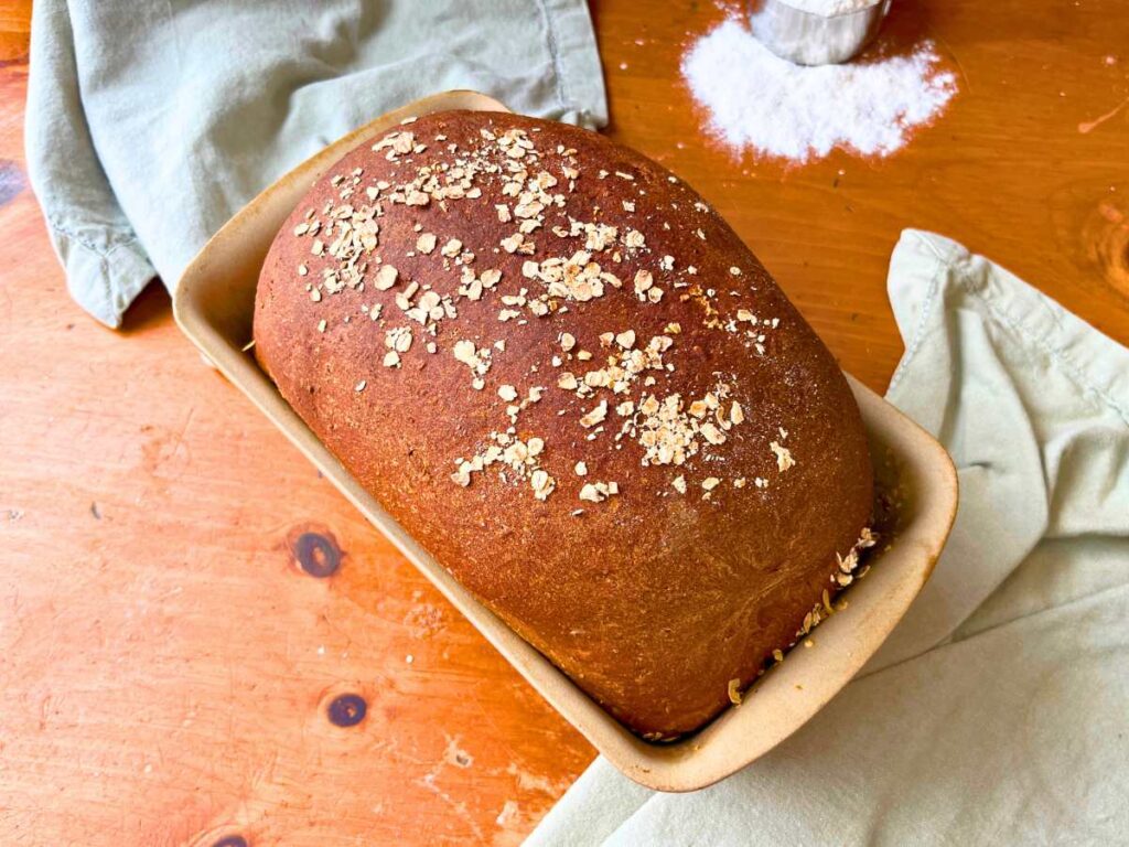 A baked loaf of Oatmeal molasses brown bread with oats on top.