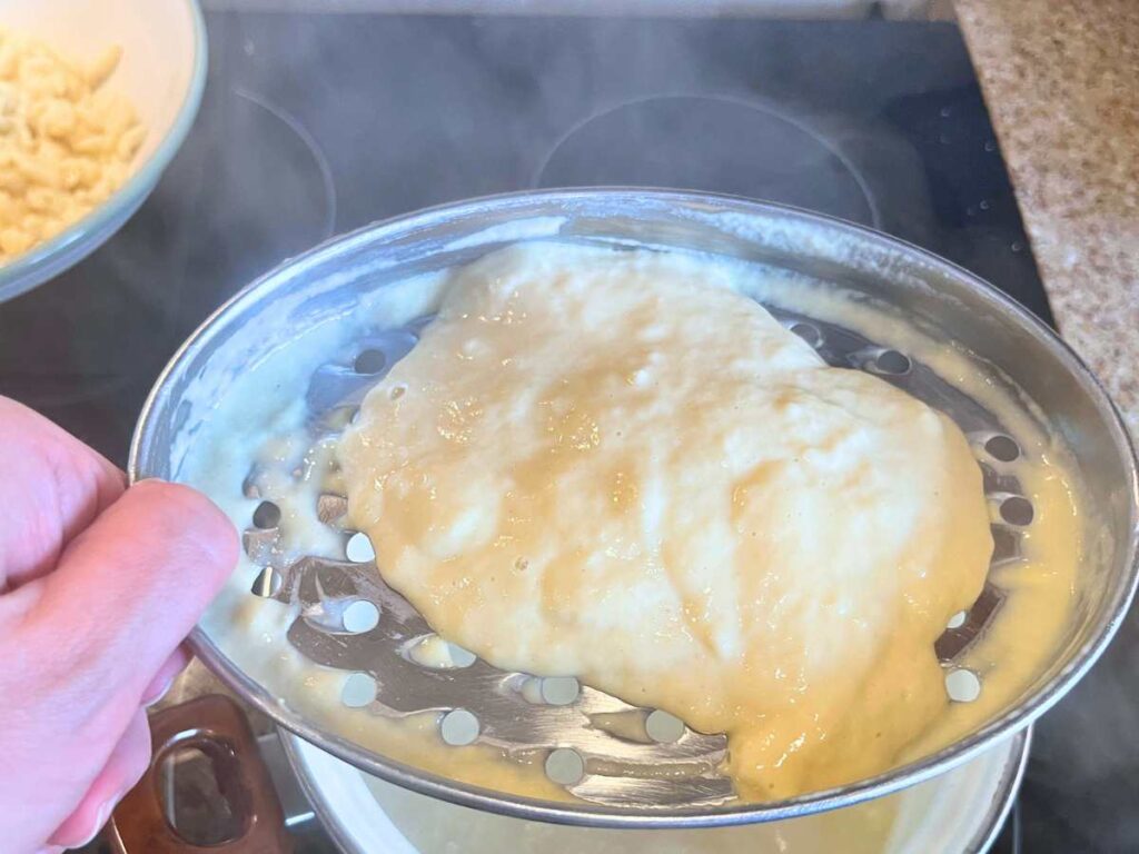 A woman is holding a cheese grater with spaetzle batter on top.