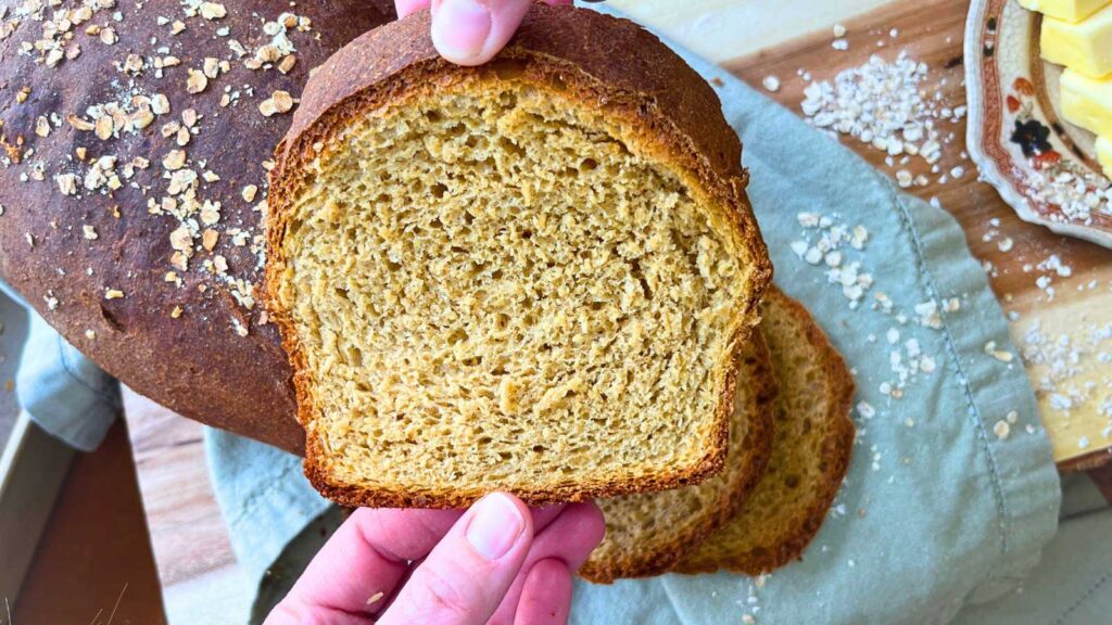 A woman is holding a slice of molasses brown bread.