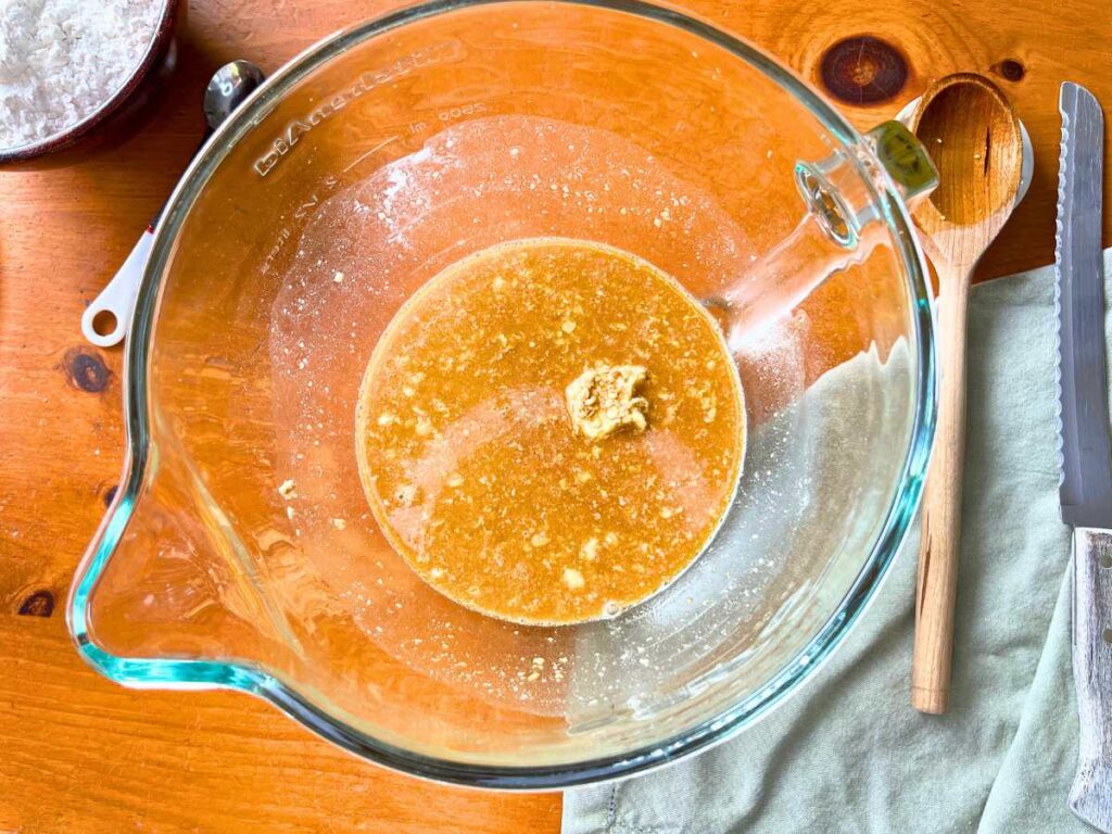 A large glass bowl with a water, yeast, and molasses mixture inside.