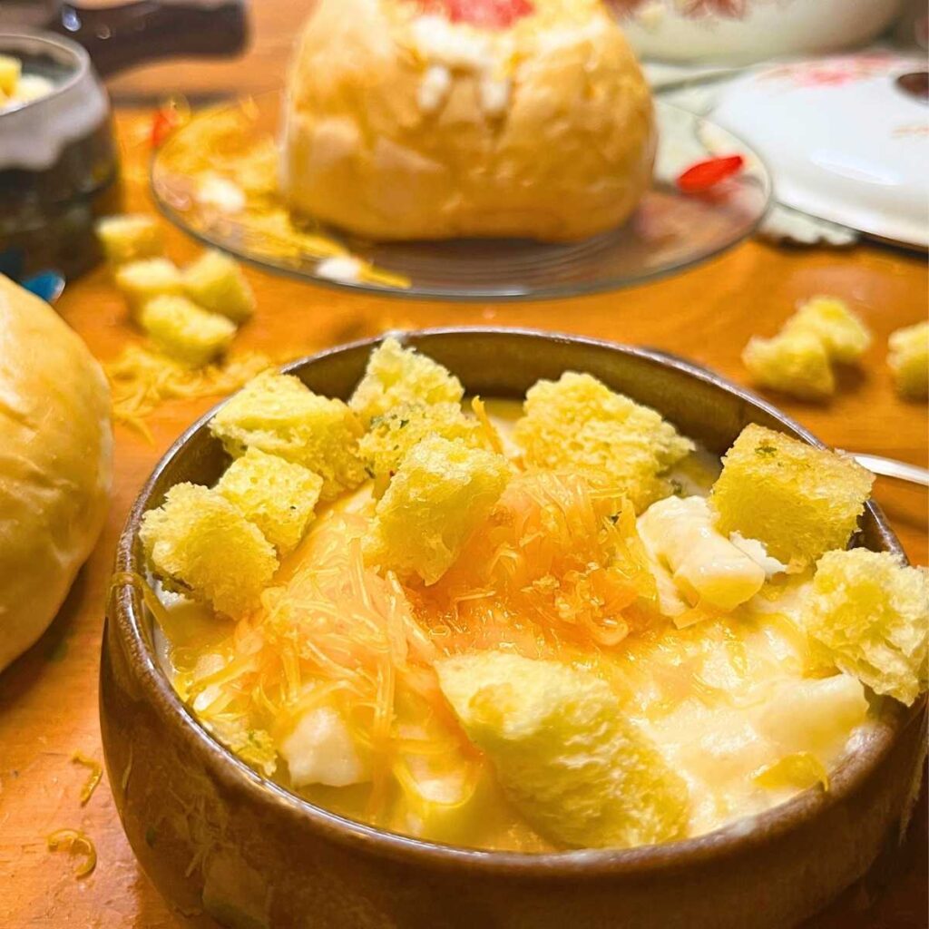 A brown bowl with potato soup inside, topped with grated cheese and croutons.