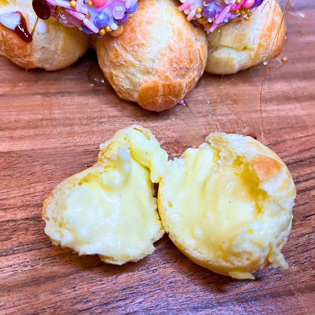 A profiterole split in half to show the pastry cream inside. There is a croquembouche in the background.