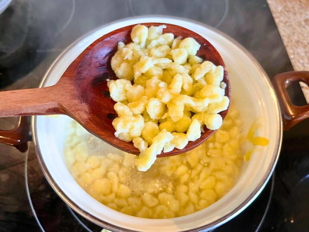 A woman holding up a slotted woman spoon with cooked spaetzle.