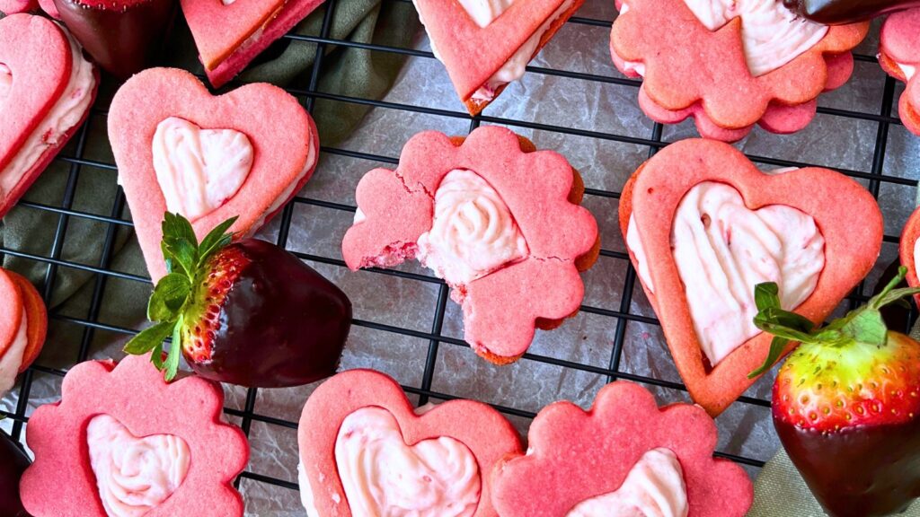 A wire rack with strawberry sandwich cookies. There are chocolate dipped strawberries.