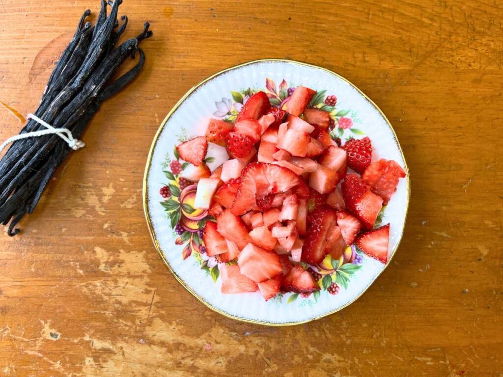 A plate with diced strawberries. There are vanilla beans of to the side.