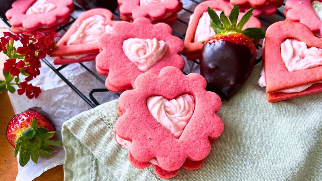 A table full of strawberry sandwich cookies. There is a chocolate dipped strawberry off to the side.