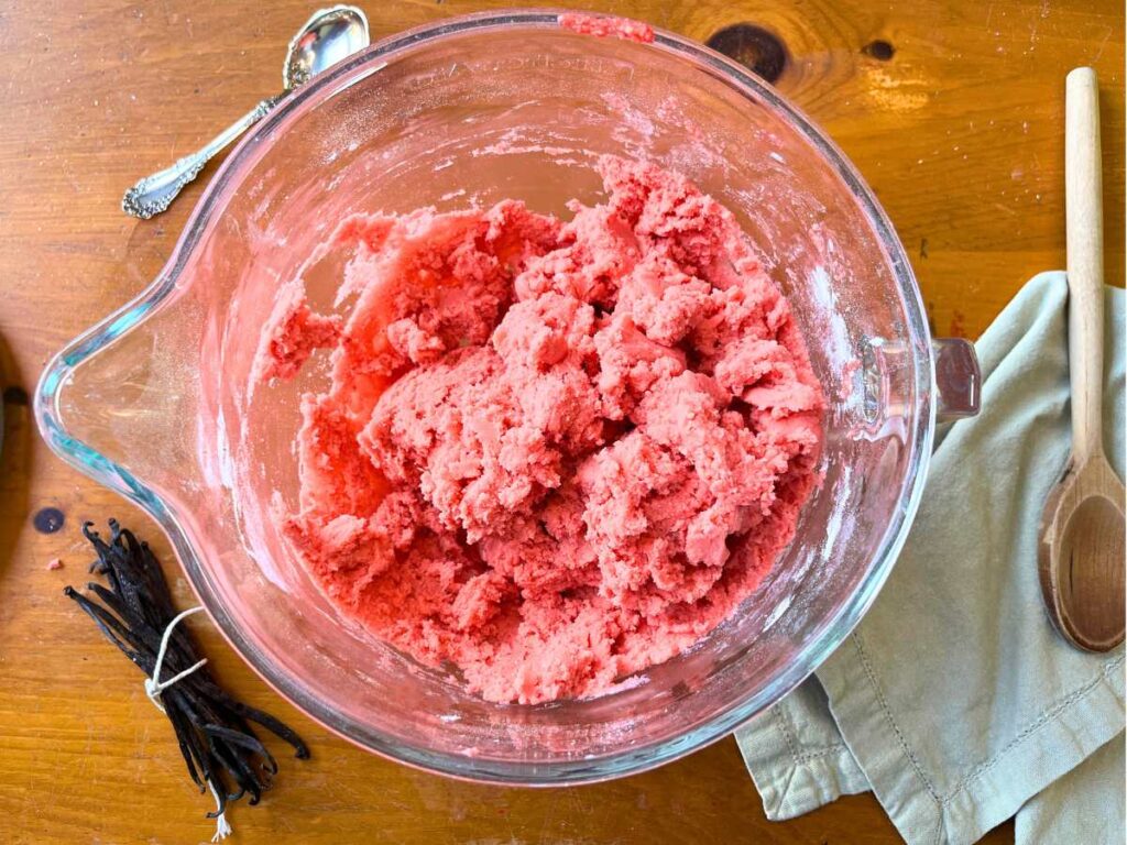 A glass bowl with pink cookie dough inside.