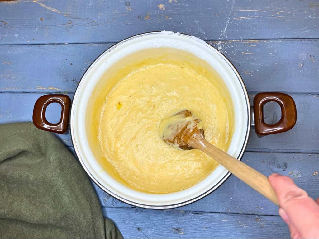 A woman stirring melted cheese fondue in a white sauce pot.