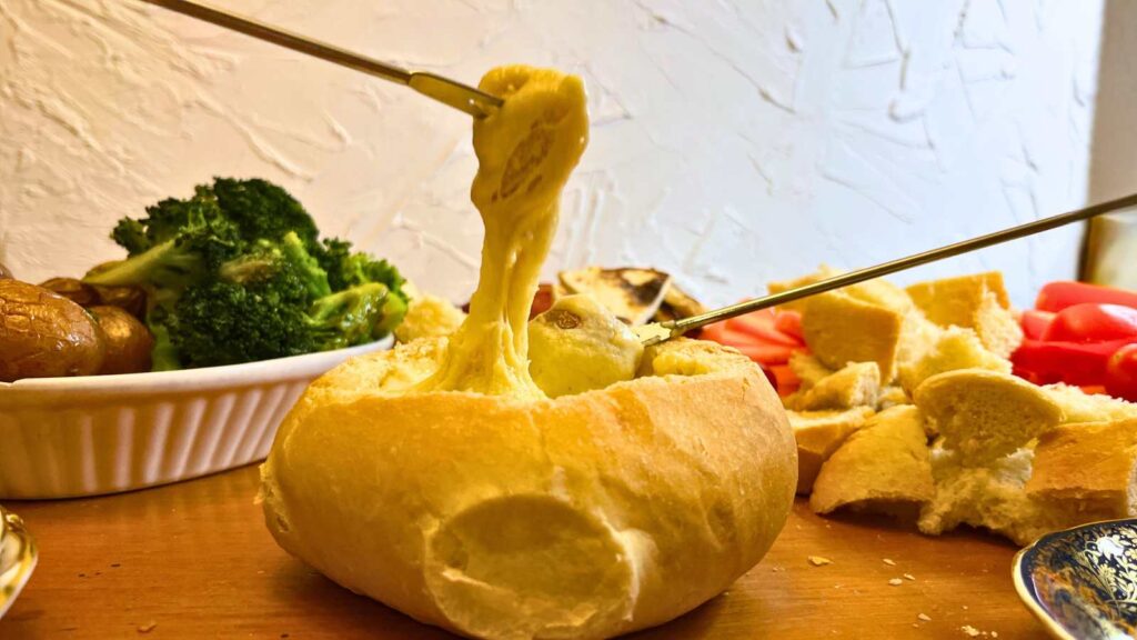 Two people are dipping things into a cheese fondue in a bread bowl.