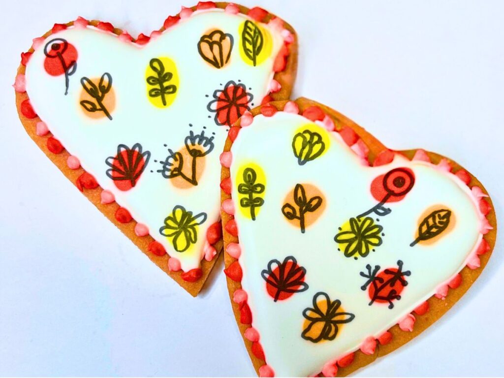 Two pink heart cookies decorated with royal icing and drawn flowers.