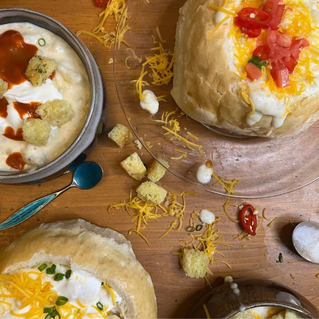 Some bowls of potato soup with different toppings. Some of the bowls are made of bread.