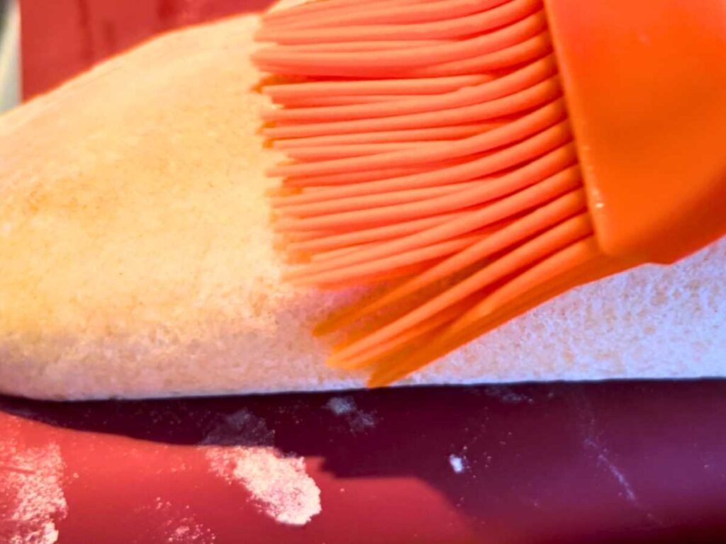 A woman brushing a loaf of bread with an orange silicone pastry brush.