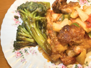 A plate of Chinese food. There is broccoli on the side and a stir fried pork and veggie dish in the main area of the plate.
