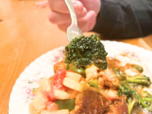 A man holding a fork with a spear of broccoli on it.  There is a plate of Chinese food in the background.