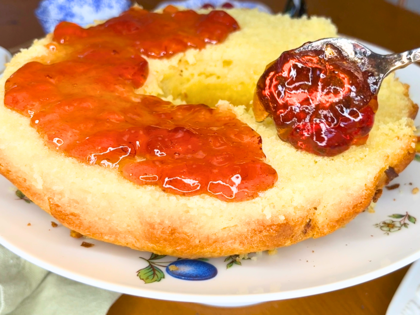 A woman spreading raspberry jelly inside of a vanilla cake.