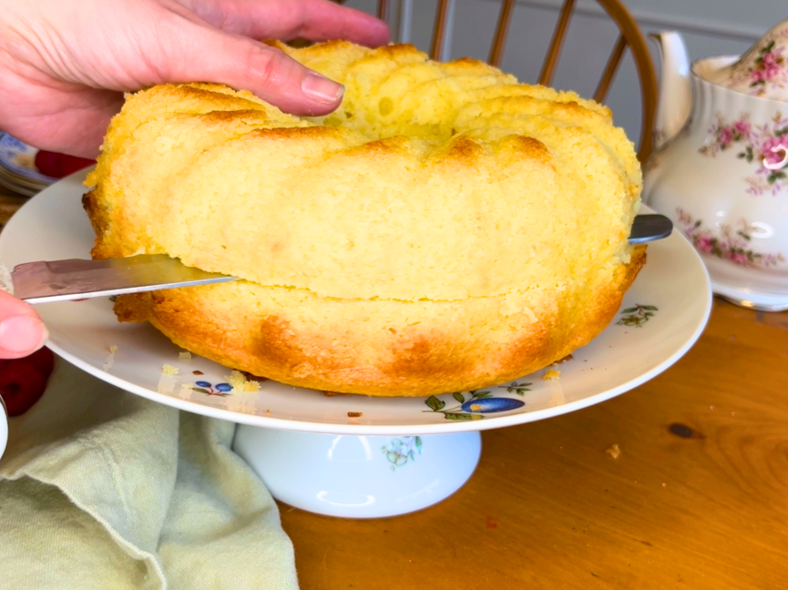 A woman cutting a circular vanilla cake in half with a bread knife