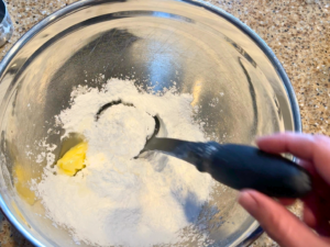 A woman mixing icing sugar and butter in a large metal bowl.