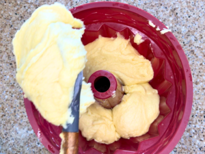 Woman spooning a white cake batter into a silicone cake mold.