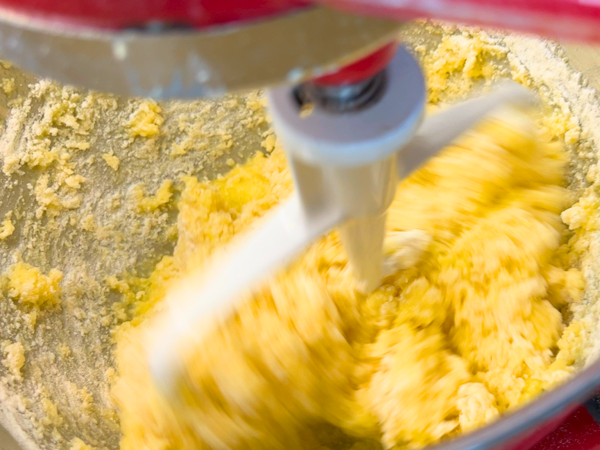 A cake batter mixing in the bowl of a stand mixer with the paddle attachment.