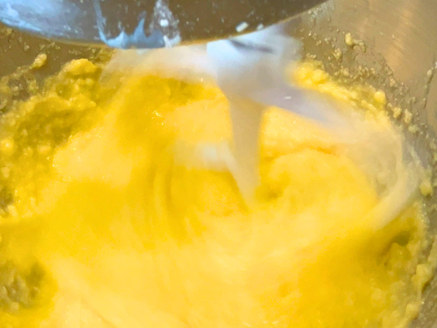 A cake batter being mixed in the bowl of a stand mixer with the paddle attachment.