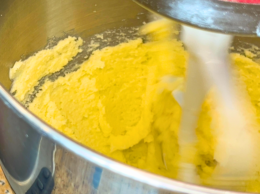 Butter and sugar being creamed in the bowl of a stand mixer with the paddle attachment.