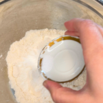 A woman adding baking powder to a flour mixture in a metal bowl