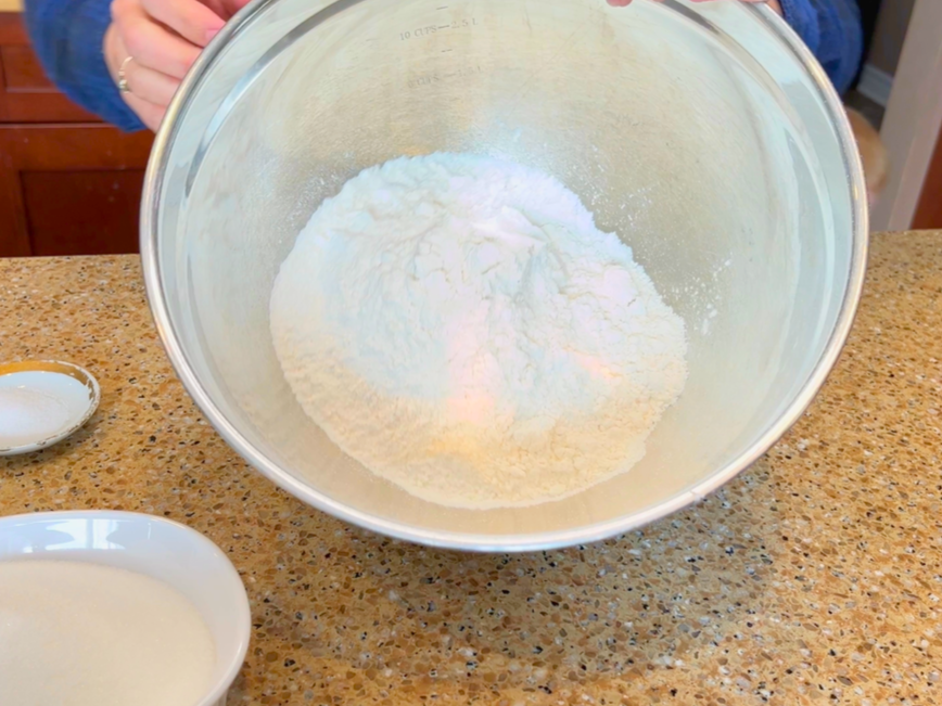 A woman holding a metal bowl with flour in it.