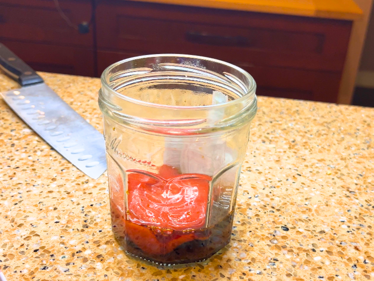 A glass jar with sugar, tamari, and ketchup in it.
