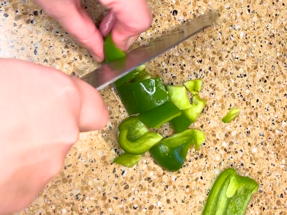 A woman chopping a green bell pepper.