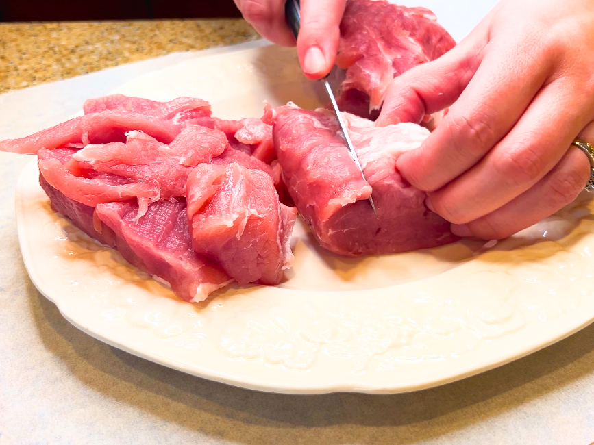 A woman cutting a pork loin into chunks.