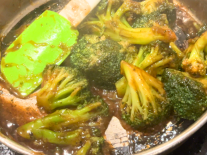 A woman stirring a frying pan with broccoli and a brown garlic sauce in it.
