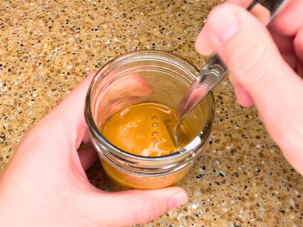 A woman stirring a brown mixture in a canning jar.