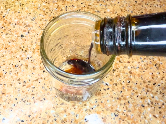 A woman pouring Tamari sauce into a mason jar.