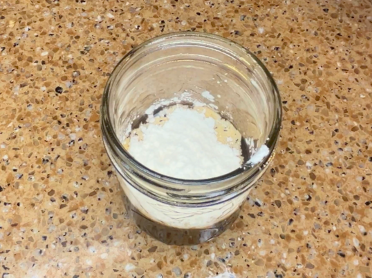 A mason jar with liquid and cornstarch on top.