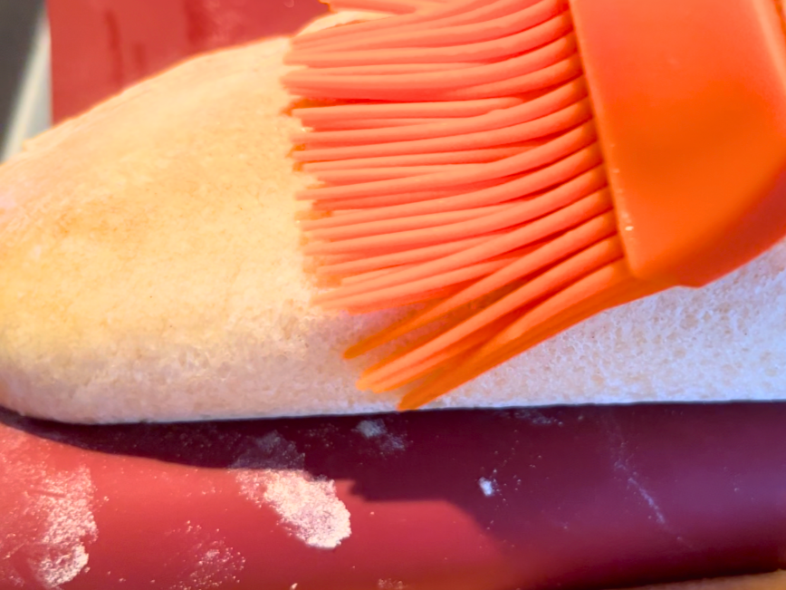 Woman brushing the top of a baguette with an orange pastry brush.