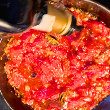 Woman adding balsamic vinegar to a pan with cooked tomatoes.