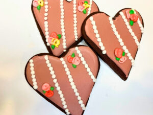 Three chocolate sugar cookies decorated with royal icing in a pearls and roses design.